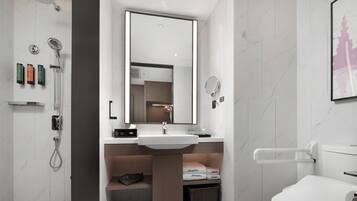 Un baño moderno con un espejo grande, un lavamanos, un inodoro y una zona de ducha.