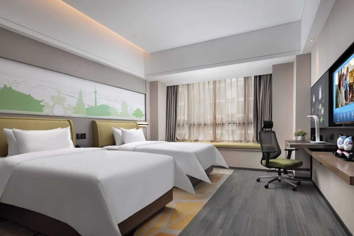 A hotel room with two beds, a desk with a computer, a TV, and a window with curtains.