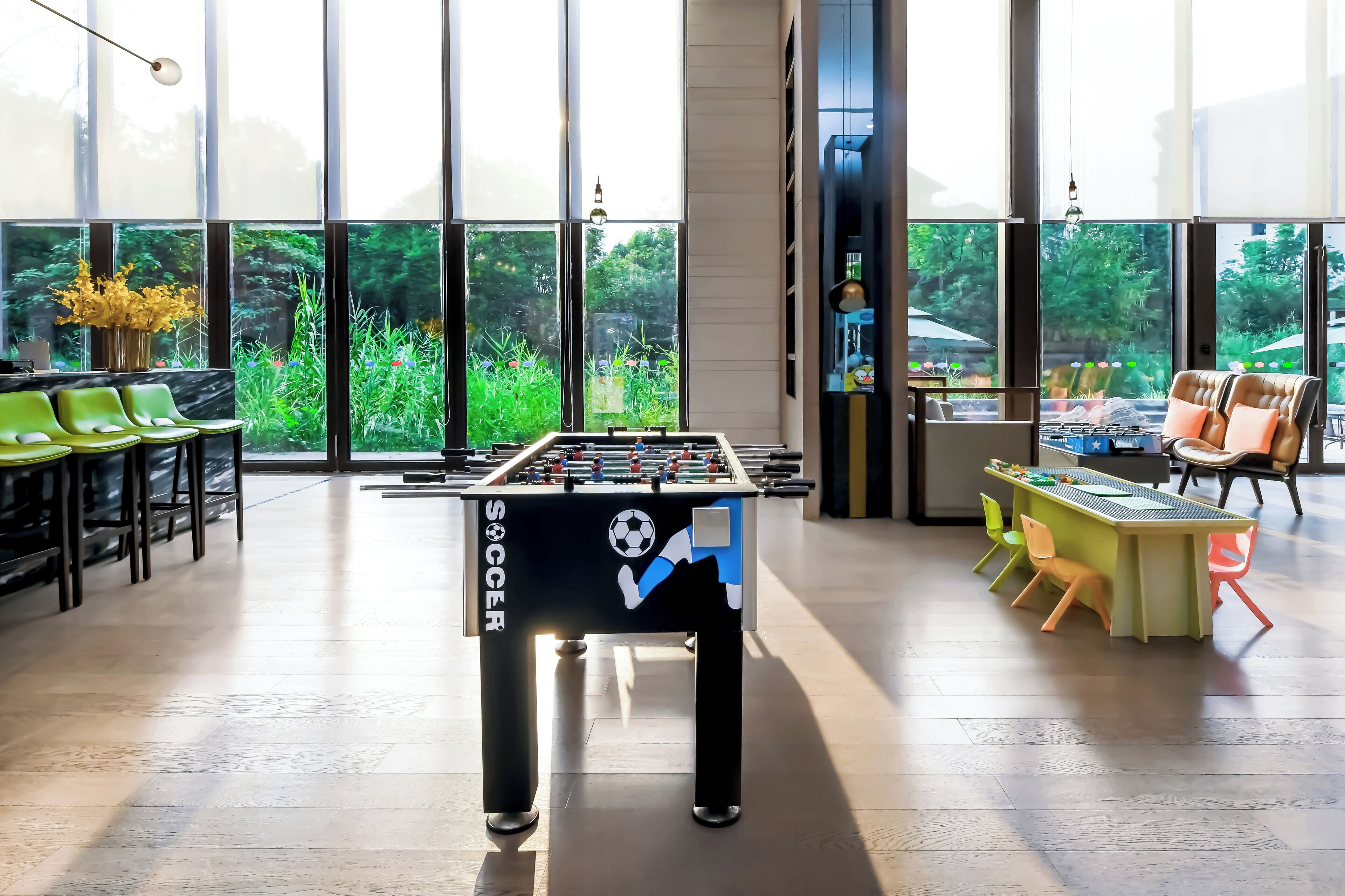 A modern indoor space with a foosball table, seating area, and large windows offering a view of greenery.