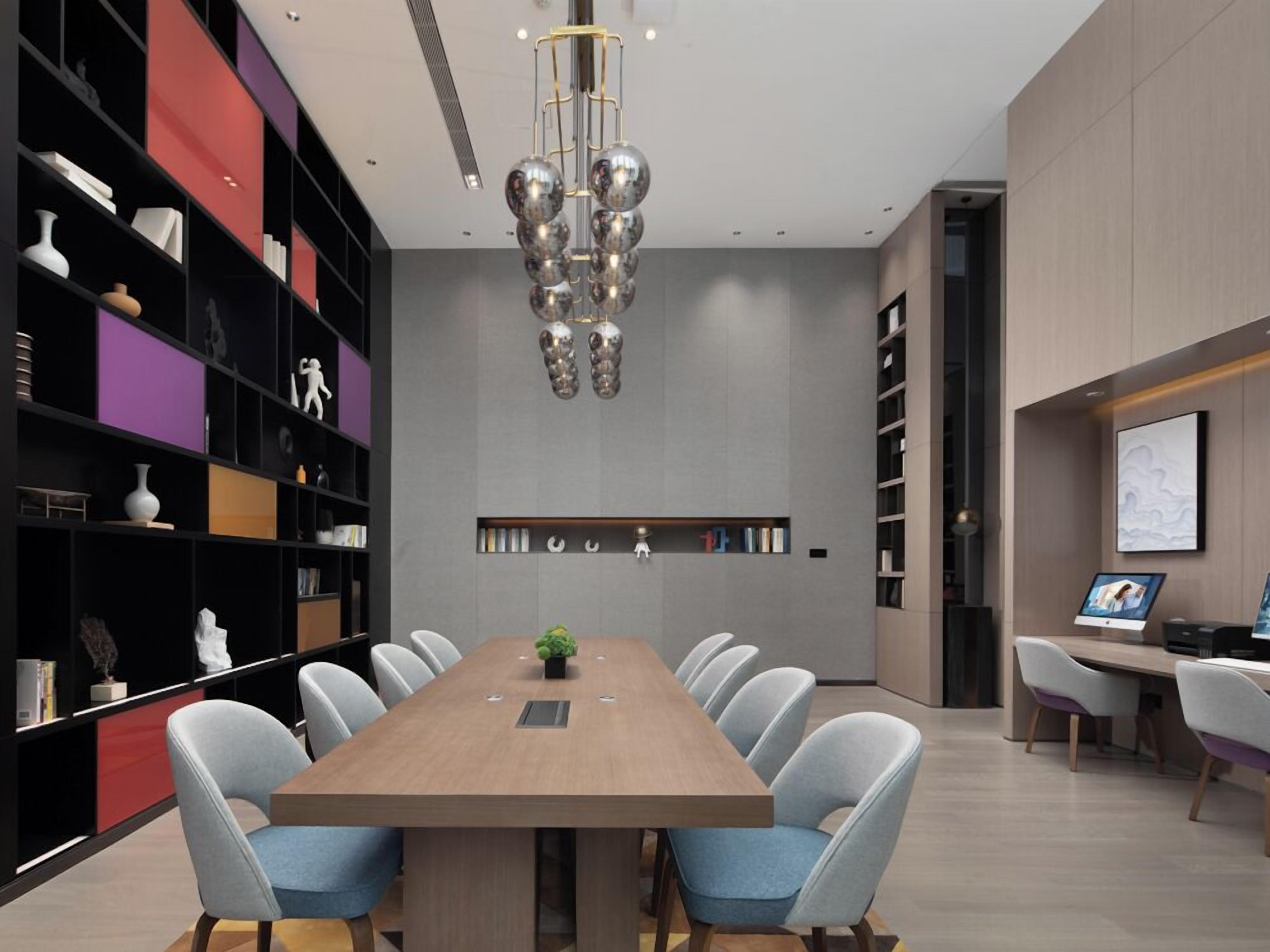 A modern conference room with a long table, light blue chairs, a central plant, and a unique chandelier.