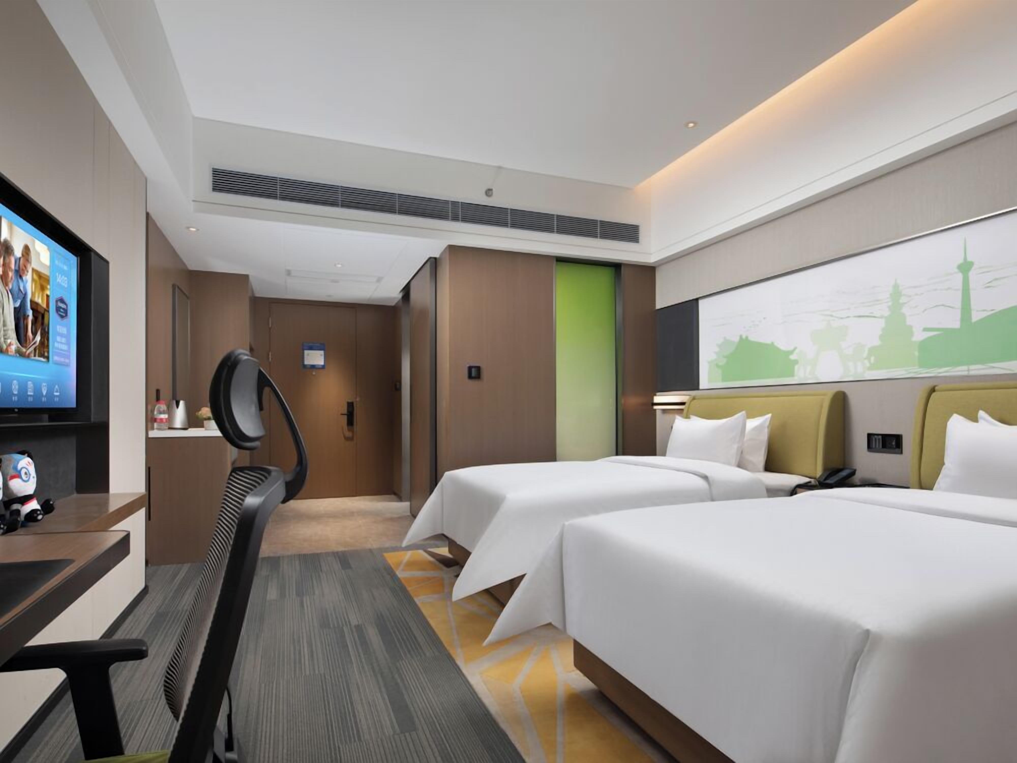 A hotel room with two beds, a desk with a chair, a television, and a large window.