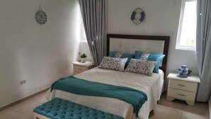 Ein Schlafzimmer mit Bett, Bank, Nachttisch, Fenster und Wandbild.
