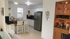Eine moderne Küche mit Kühlschrank, Esstisch und Stühlen. Ein Holzschrank mit Weinflaschen ist ebenfalls vorhanden.