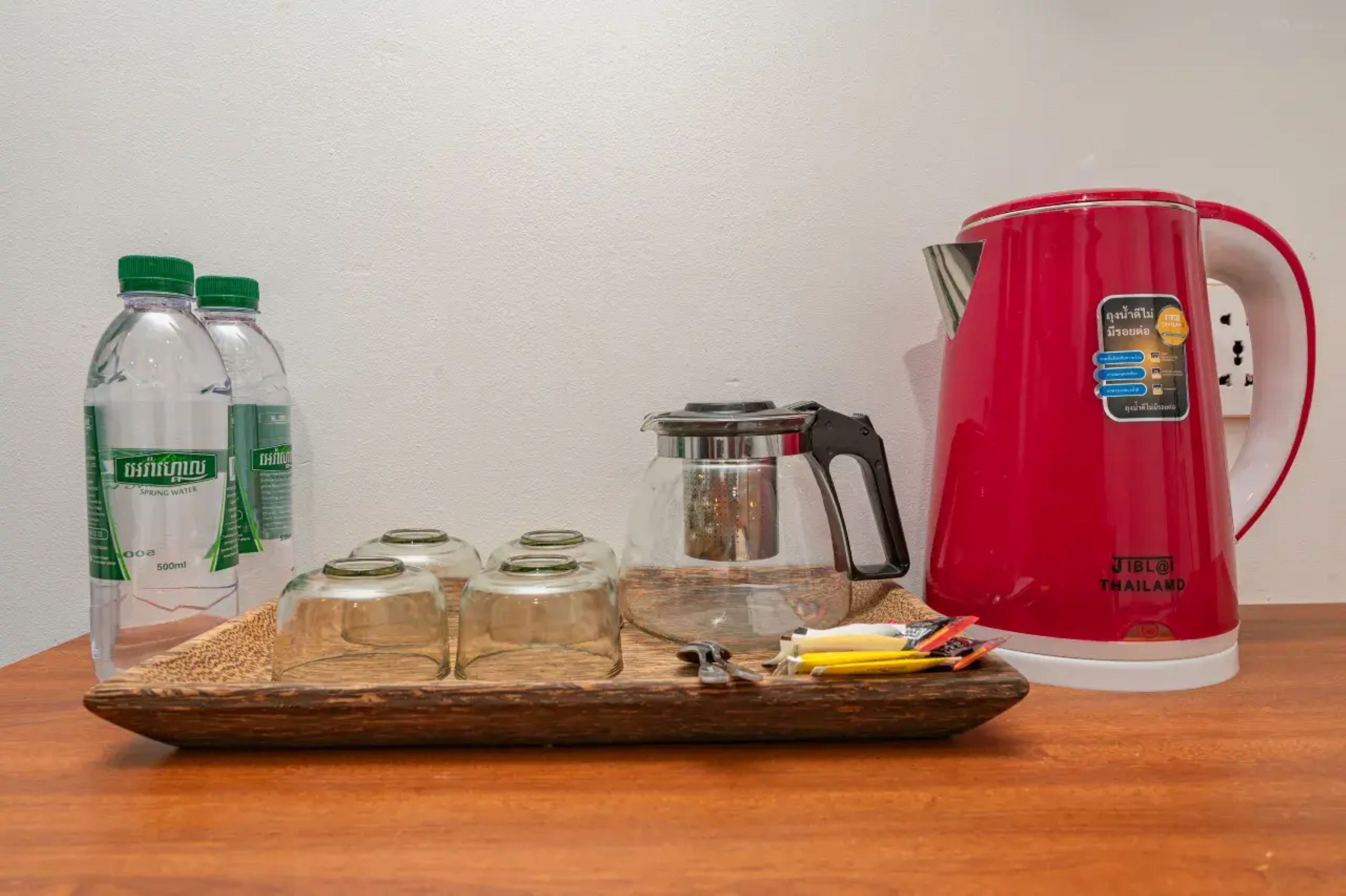 Une table sur laquelle se trouvent une bouilloire électrique rouge, deux bouteilles d’eau et deux bocaux en verre.