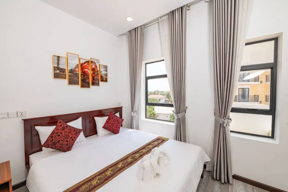 A hotel room with a large bed, a view of the outside, and three framed pictures on the wall.