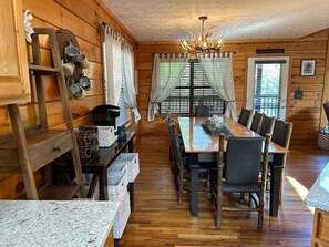 A wooden cabin interior with a dining table, chairs, a chandelier, and a 'Welcome Friends' sign. - Firefly Landing, 4 BR Cabin, Hot-tub, Community Pool, DollyWood (Sevierville)