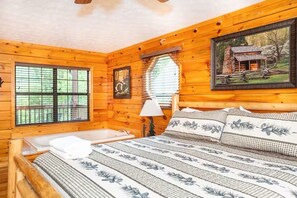 A wooden cabin bedroom with a bed, a window, a painting, and a lamp. - Firefly Landing, 4 BR Cabin, Hot-tub, Community Pool, DollyWood (Sevierville)