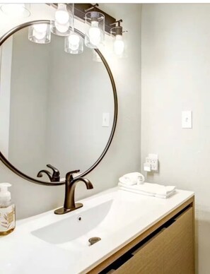 A bathroom with a large round mirror, a sink, and a towel rack. - Birdie Bungalow is a charming home on the 13th hole of the golf course. (Conroe)
