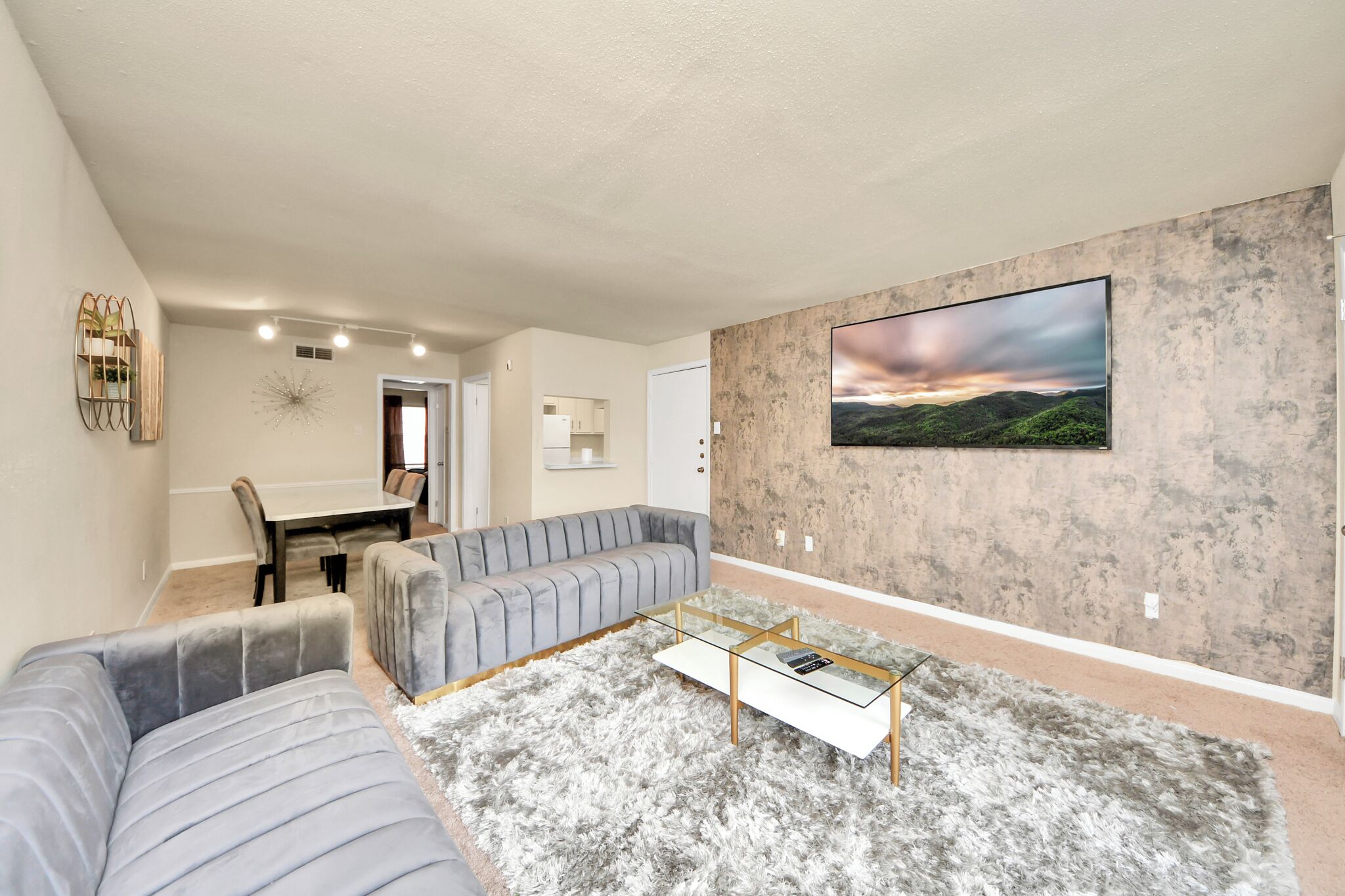 Un salon moderne avec un canapé gris, une table basse en verre et un grand tableau représentant un paysage accroché au mur.