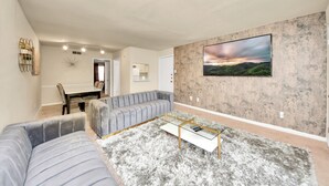 A modern living room with a grey sofa, a glass coffee table, and a large landscape painting on the wall. - Houston Galleria Suite 
Modern Rental 5 mins from the Galleria Mall (Houston)