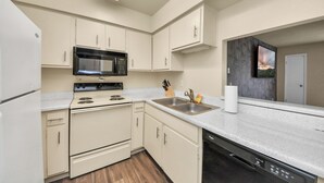 A compact kitchen with white cabinets, a stainless steel microwave, a stove, and a dishwasher. - Houston Galleria Suite 
Modern Rental 5 mins from the Galleria Mall (Houston)