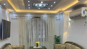 Una sala de estar con dos sillones, una mesa de centro, un tapete estampado, un televisor montado en la pared y un equipo de aire acondicionado.
