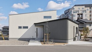 A modern building with a flat roof, a small entrance, and a gravel driveway.