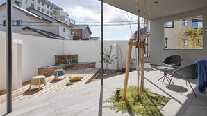 A modern outdoor patio with a wooden deck, seating area, and a small garden.