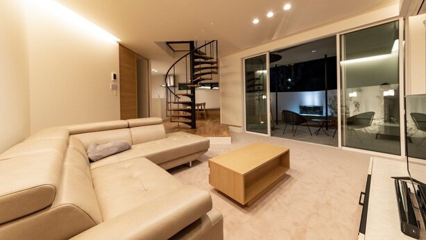 A modern living room with a beige sectional sofa, a wooden coffee table, and a spiral staircase leading to an upper level.