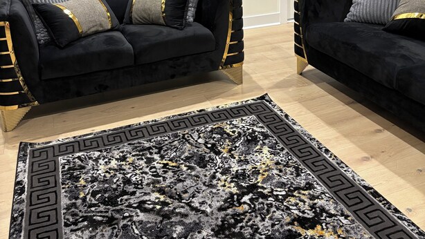A living room with two black sofas, a patterned rug, and four framed artworks on the wall.