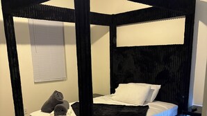 A four-poster bed with a black frame, white bedding, and a dark throw blanket.