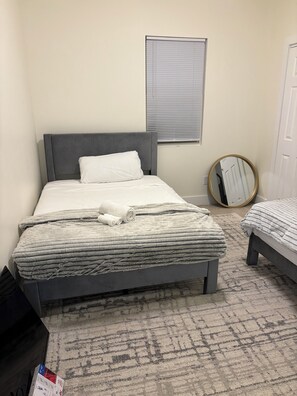 Quarto com cama, janela com persianas, espelho redondo e piso coberto por carpete.