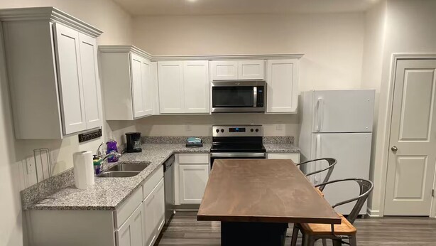 A modern kitchen with white cabinets, a granite countertop, a wooden table, and a stainless steel refrigerator.