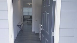 A hallway leading to a room with a door, a bench, and a window with blinds.