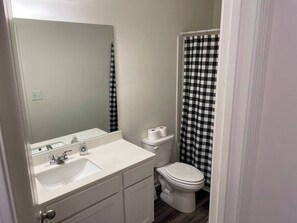 Un baño con lavamanos blanco, un espejo, un inodoro y una cortina de ducha a cuadros.