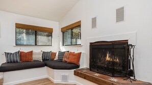 A cozy living room with a built-in bench, large windows with blinds, a fireplace, and a wooden bench with decorative tiles.