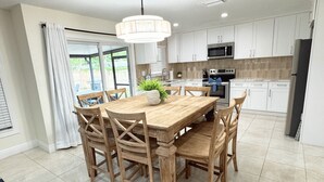 Une cuisine moderne avec des meubles blancs, une table à manger en bois et un luminaire suspendu.