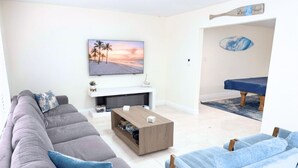Un salon avec un canapé gris, un canapé bleu, une table basse et un tableau représentant une scène de plage.