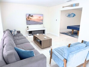 Ein Wohnzimmer mit einem grauen Sofa, einem blauen Sofa, einem Couchtisch und einem Bild von einer Strandansicht.