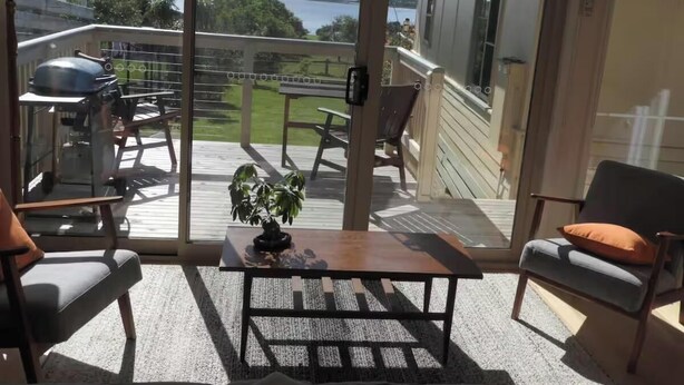 En balkon med udsigt over et søområde, møbleret med stole og et bord, samt en grill.