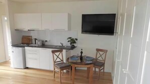 Et kompakt køkken med hvide skabe, en indbygget ovn og et spiseområde med et bord dækket til to.