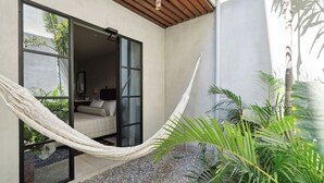 Un hamac dans une pièce dotée d’une grande fenêtre, d’un lit et donnant sur un jardin.