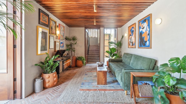 Un salon chaleureux avec un plafond en bois, un canapé vert, une table basse et divers tableaux encadrés accrochés aux murs.