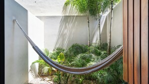 Una hamaca en un jardín con diversas plantas y una pared blanca.