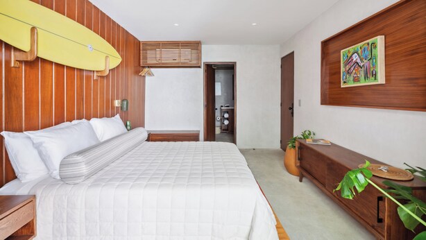 Una camera da letto con un letto, pannelli di legno, una tavola da surf, un quadro e una pianta.