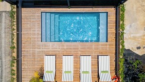 A rectangular swimming pool with a wooden deck surrounding it, four lounge chairs with striped cushions, and a small waterfall feature. - ALMA Surf Lodge Terrace Queen with View (Corral del Risco)