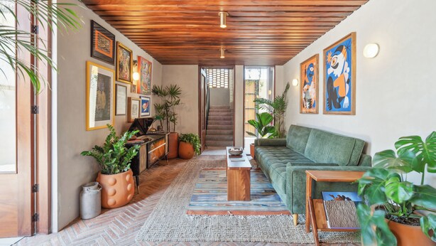 A cozy living room with a wooden ceiling, a green sofa, a coffee table, and various framed artworks on the walls. - ALMA Surf Lodge Terrace Queen with View (Corral del Risco)