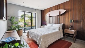 Ein modernes Schlafzimmer mit einem großen Bett, einer Holzwand, einem Surfbrett und Blick auf Grünfläche.