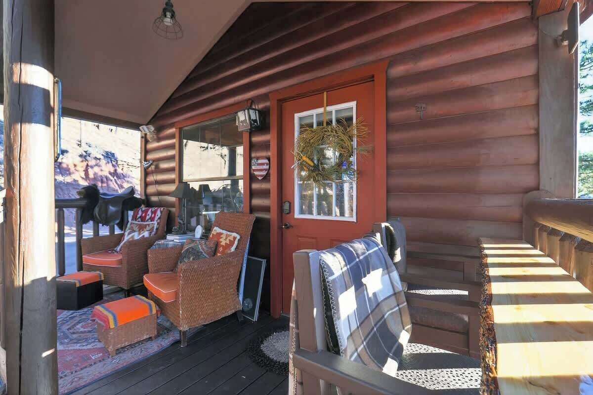 A wooden cabin with a porch, wicker furniture, and a red door.