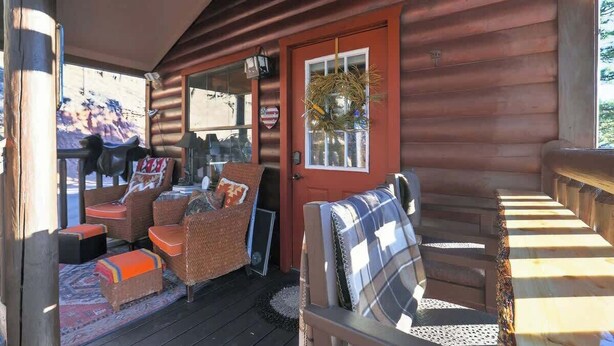 A wooden cabin with a porch, wicker furniture, and a red door. - Hummingbird Heaven! Woodland Park Mountain Cabin (Woodland Park)