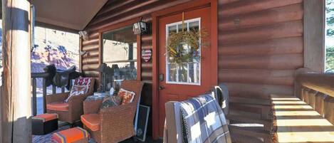 A wooden cabin with a porch, wicker furniture, and a red door.