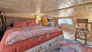 A cabin interior with a large bed, wooden walls, and a small desk area. - Hummingbird Heaven! Woodland Park Mountain Cabin (Woodland Park)