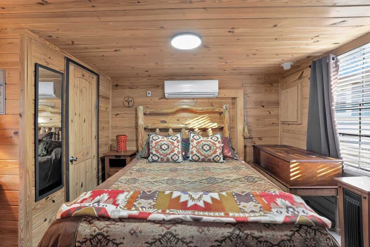 A wooden room with a bed, a nightstand, a dresser, and a window with blinds.