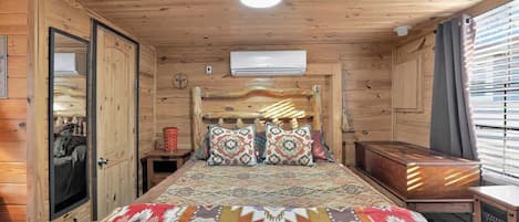 Una habitación de madera con cama, mesita de noche, cómoda y ventana con persianas.