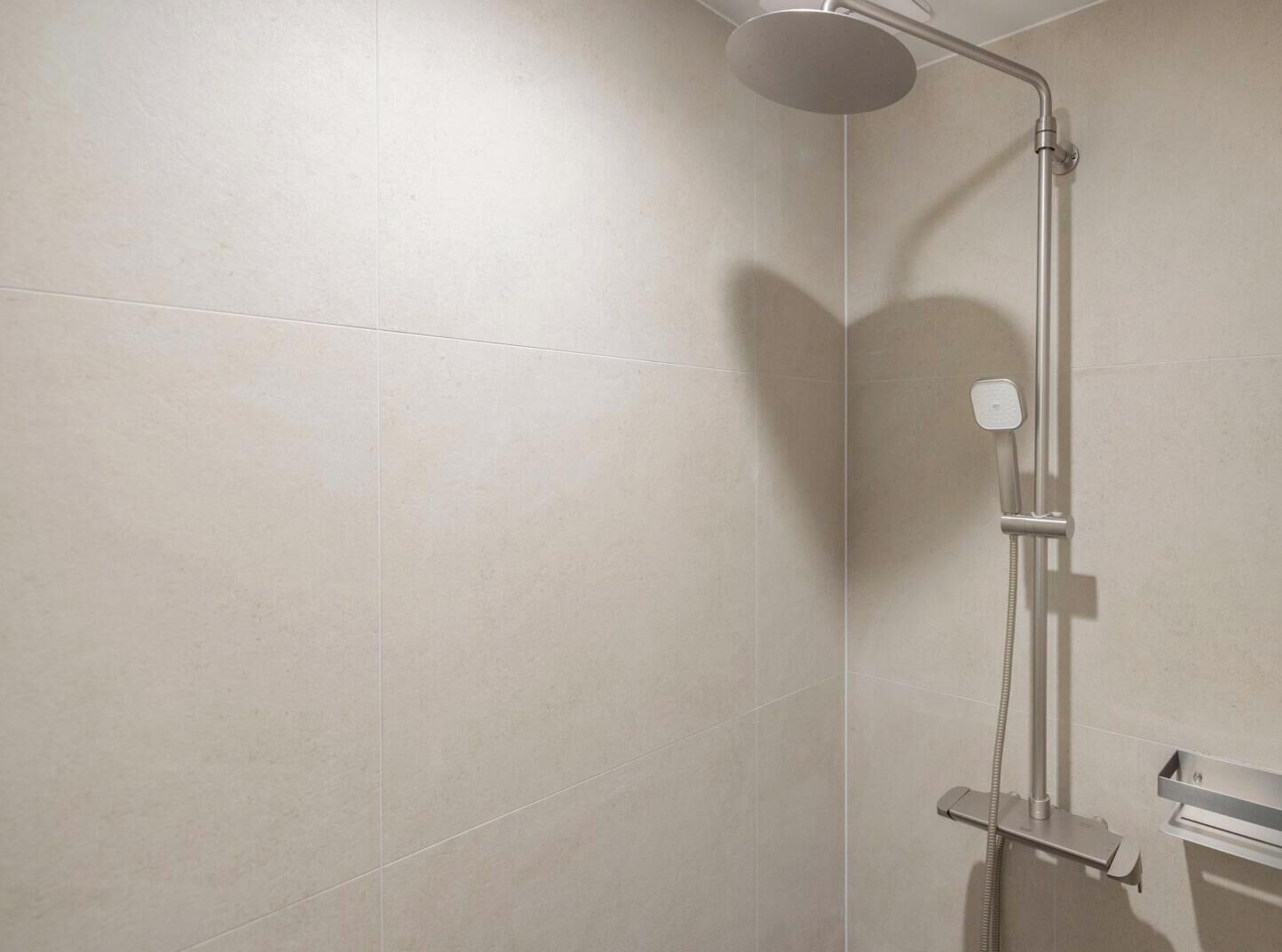 Ducha moderna con cabezal de ducha de mano y panel de control en la pared.