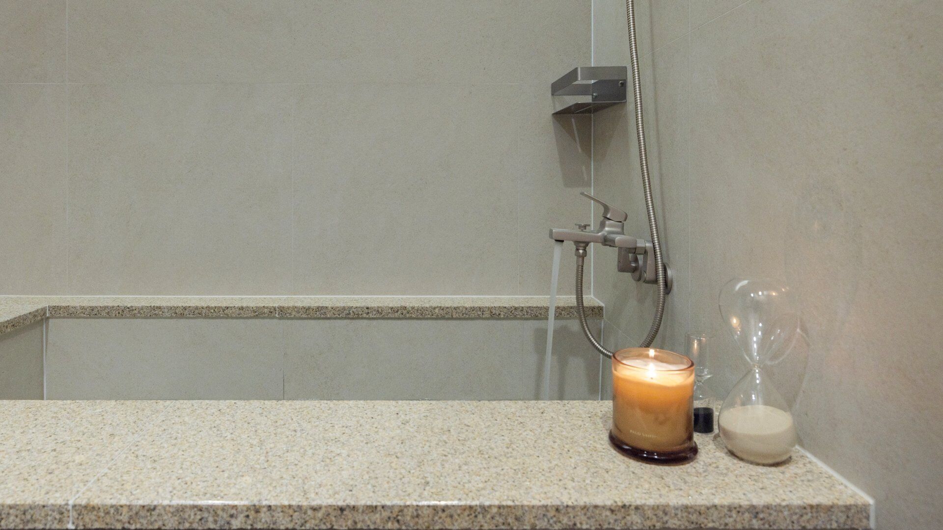 A bathroom with a shower, a candle, and a glass container on the counter.