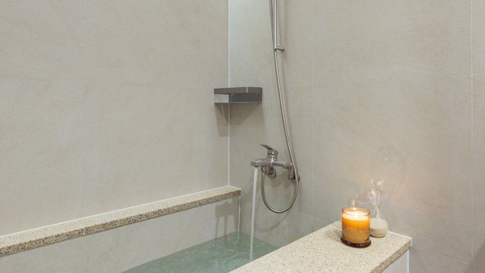 Un espace douche doté d’une paroi en verre, d’un pommeau de douche à main et d’une bougie posée sur le comptoir.