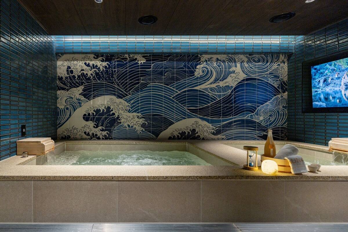 A hot tub with a traditional Japanese wave pattern wall behind it, a caution slipper sign, and a bottle of sake on the side.