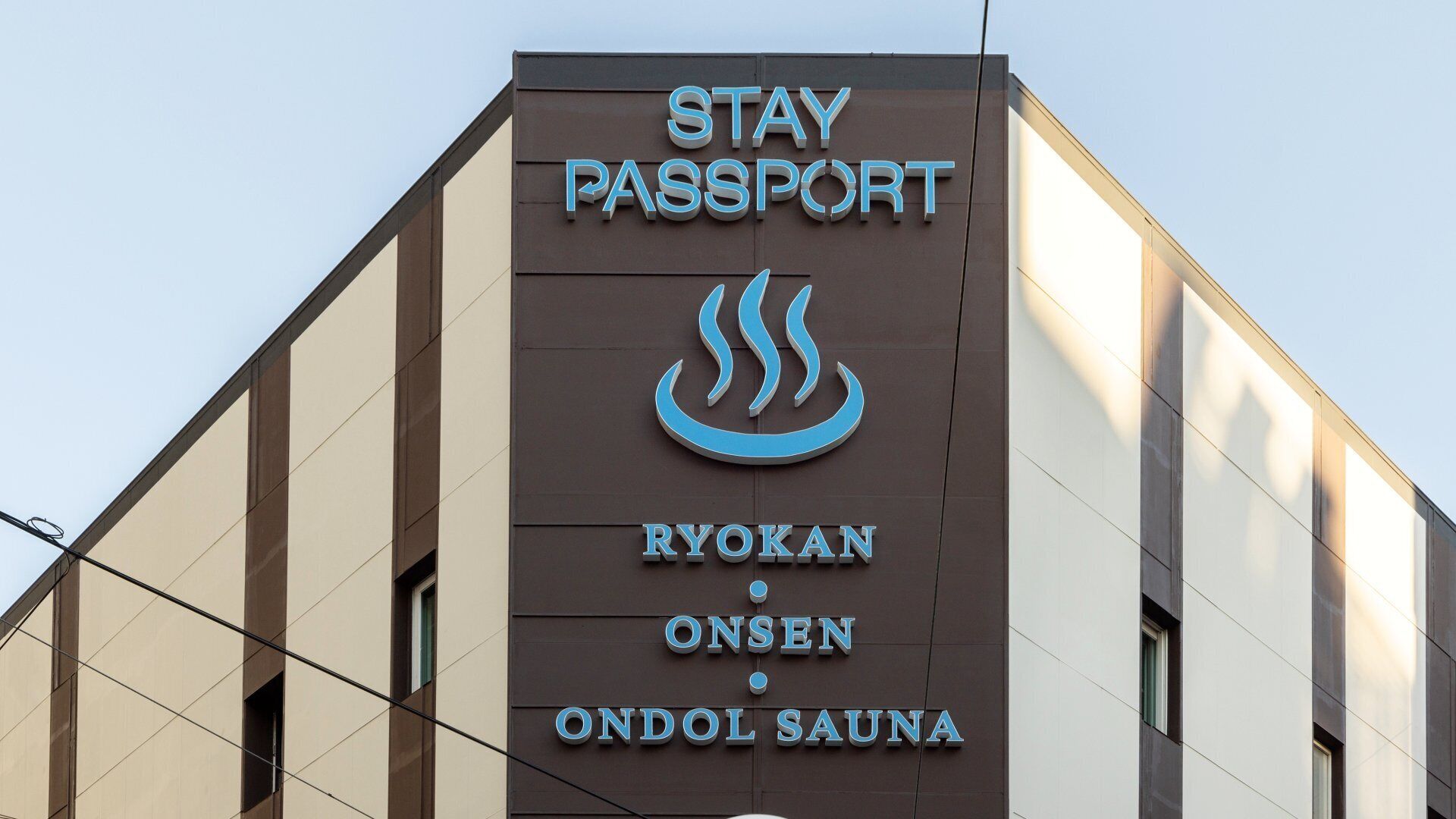 Un bâtiment sur lequel on peut lire l’inscription suivante : « STAY PASSPORT RYOKAN ONSEN ONDOL SAUNA ».