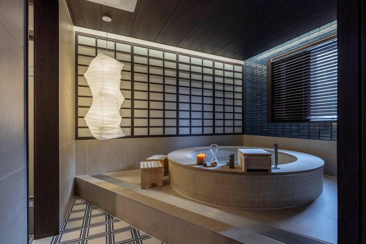 A modern bathroom with a freestanding bathtub, a large paper lantern, and a window with blinds.